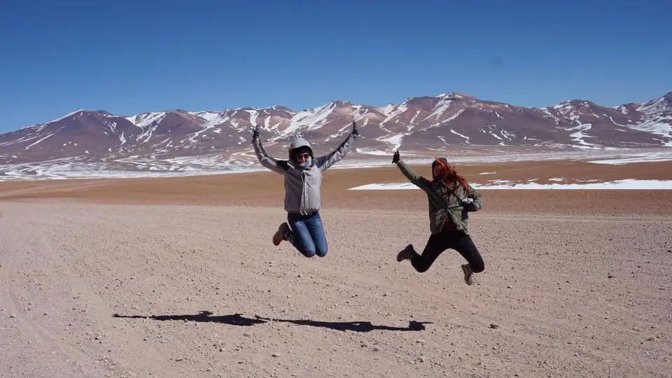 two solo female travellers jumping in the air in front of snow capped mountains