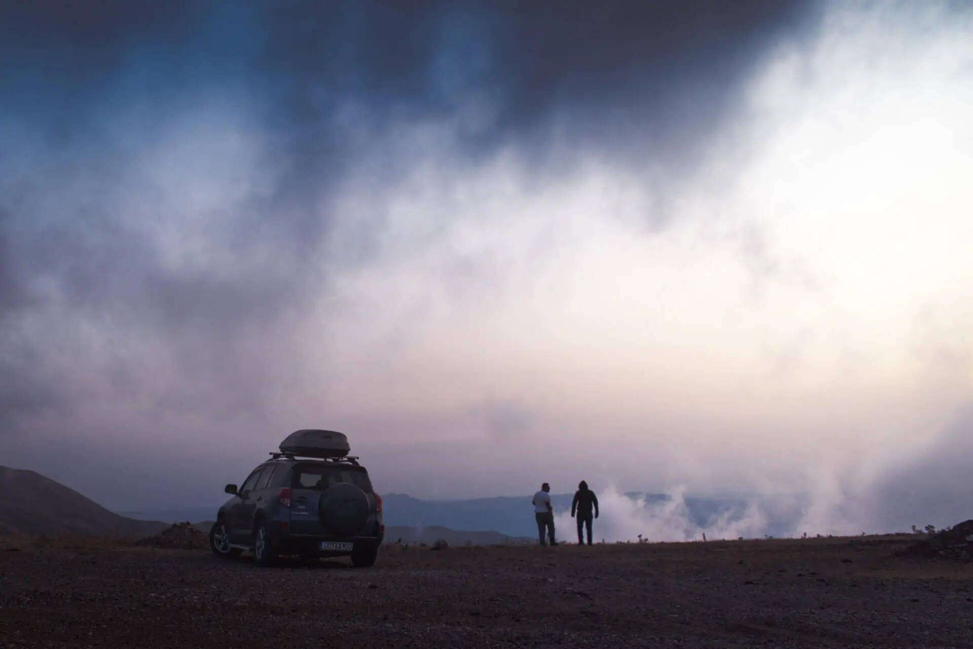 A travelling couple stand by their rental car on a misty morning in Greece