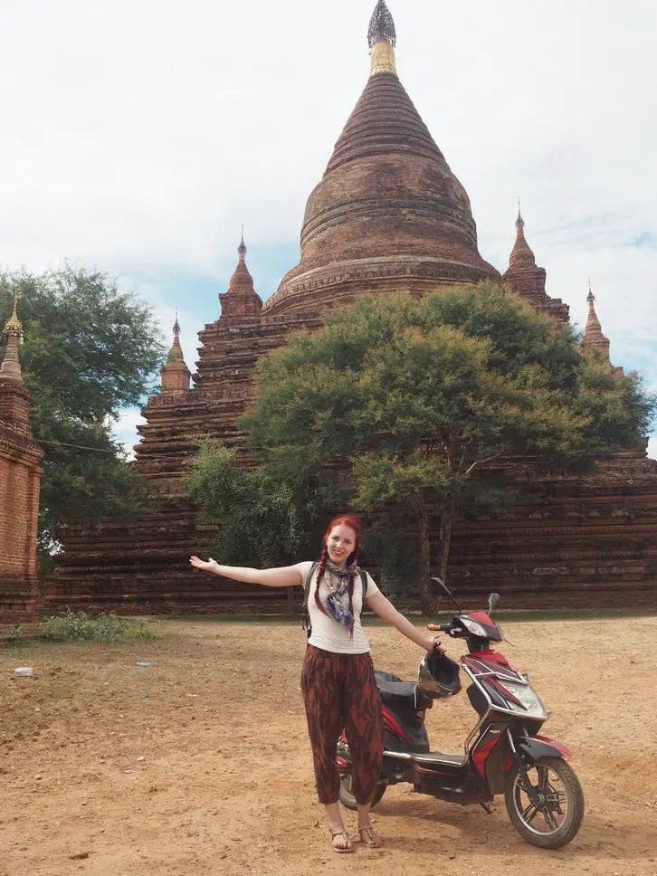 solo female traveller with a scooter in front of a temple in Myanmar